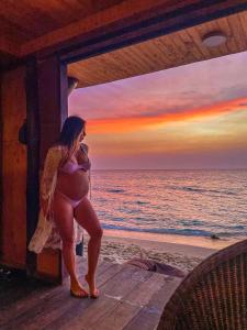Hotel Prana Beach في بارو: امرأة حامل تقف على الشاطئ عند غروب الشمس