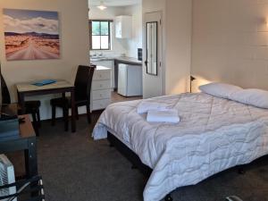 a bedroom with a bed and a desk and a kitchen at Stonehaven Motel in Whangarei