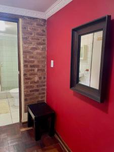 a bathroom with a red wall with a mirror and a stool at Timebridge Mansions in Johannesburg