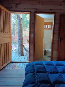 1 dormitorio con cama y puerta a un árbol en Cabaña en el bosque de punta del diablo, en Punta del Diablo
