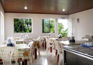 un restaurante con sillas blancas, mesas y ventanas en Finca Hotel Villa Gladys en Mesitas del Colegio en El Colegio