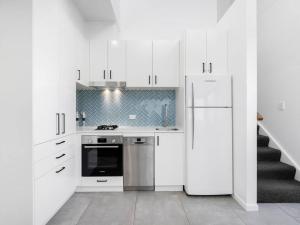 a white kitchen with a refrigerator and a staircase at 1 Bedroom Modern Townhouse in Casuarina in Casuarina