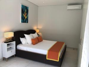 a bedroom with a bed with white sheets and orange pillows at Montecrista Appart moderne et cosy, 1 chambre à 2 min plage Pereybere in Pereybere