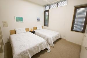 two beds in a room with white walls and windows at 癒しの空間 One Earth in Akamine