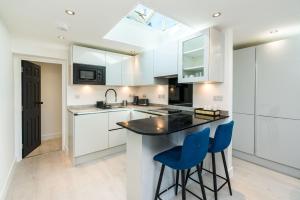 a kitchen with white cabinets and blue bar stools at Spacious Modern 2 Bedroom London Flat in Sydenham