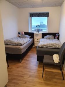 a bedroom with two beds and a chair and a window at Fælleshuset Kirkebakken in Otterup