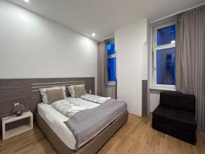 a bedroom with a bed and a chair and two windows at Vienna City Apartment 7 in Vienna
