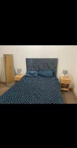 a bedroom with a bed with a blue bedspread and two tables at Beautiful 1 bedroom flat in Leeds