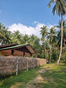 a building with a fence and palm trees at Ban Tai - Nice house in a quiet area 2 min from main road in Thongsala