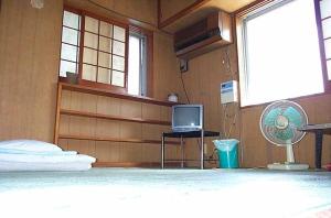 1 dormitorio con 1 cama, TV y ventilador en Guest House Green House, en Naha