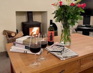 two glasses of wine and books on a table with a fireplace at Norwood Cottage in Kirkby Lonsdale