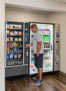 Un uomo in piedi di fronte a un distributore di bibite gassate di WoodSpring Suites Omaha Bellevue, an Extended Stay Hotel a Bellevue