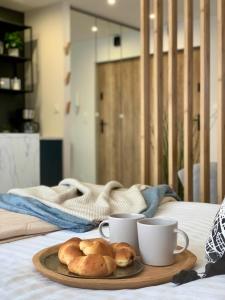 a tray with two cups and some bread on a bed at Apartament Botanica - Blisko parku i centrum - by SpaceApart in Jelenia Góra