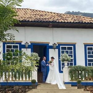 una sposa e uno sposo in piedi fuori da una casa blu e bianca di Linda Fazenda Centenária a Santa Rita do Sapucaí