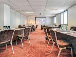 une salle de conférence avec des tables, des chaises et un écran dans l'établissement Mercure Paris Ivry Quai De Seine, à Ivry-sur-Seine