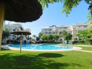 a swimming pool with an umbrella and a building at Residencial Duquesa Ground Floor Apartment in San Luis de Sabinillas