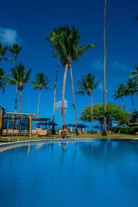 a woman sitting next to a swimming pool with palm trees at Baía Branca Beach Resort in Tamandaré