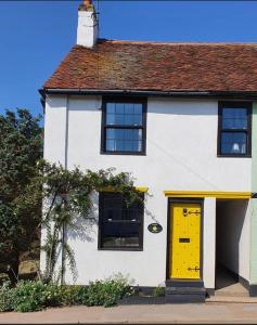 a white house with a yellow door on a street at Wayside Cottage in Saint Osyth