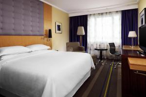 a hotel room with a large white bed and a desk at Sheraton Brussels Airport Hotel in Zaventem