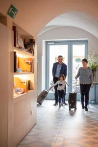 two adults and a child walking through a room with luggage at Boutique Hotel de la Ville in Laigueglia