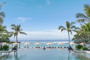 a swimming pool with palm trees and the ocean at The Ritz-Carlton Bali in Nusa Dua