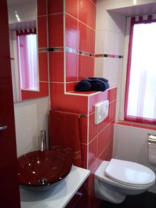 La salle de bains est pourvue d'un lavabo rouge et de toilettes. dans l'établissement Au Bercail, à Gérardmer