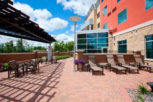 un patio avec des chaises et des tables en face d'un bâtiment dans l'établissement Courtyard Minneapolis Maple Grove Arbor Lakes, à Maple Grove