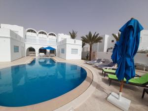 einen Pool mit Stühlen und einem blauen Sonnenschirm in einem Resort in der Unterkunft Villa La Palmeraie d'Arkou, grande piscine in Arkou