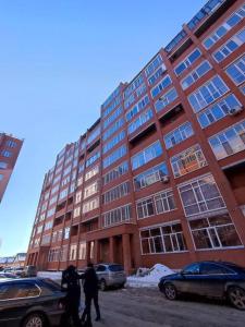 a large brick building with people walking in front of it at Апартаменты в новостройке по Байзакова 131/1 in Pavlodar