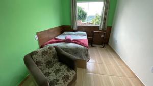 a bedroom with a bed and a chair and a window at Cantinho do sossego in Blumenau