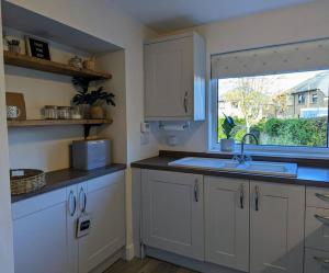 eine Küche mit weißen Schränken, einem Waschbecken und einem Fenster in der Unterkunft Parkview Cottage - Lovely home overlooking park in Carnoustie