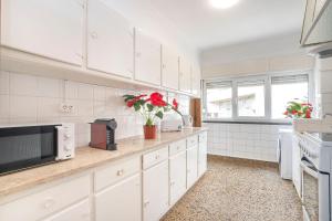 a kitchen with white cabinets and red flowers on the counter at Happy Holiday Cascais - Home in Cascais +11 photos