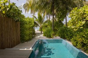 a swimming pool in front of a resort with palm trees at Avani Plus Fares Maldives Resort in Baa Atoll