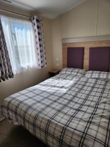 um quarto com uma cama com um cobertor xadrez e uma janela em 4 BEDROOMS CARAVAN at Waterside Leisure Holiday Park em Skegness