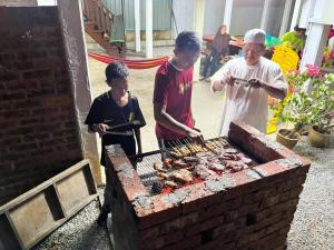 un homme et deux garçons cuisinant de la nourriture sur un grill dans l'établissement Inap Nekmi Kuala Terengganu With Pool, à Kuala Terengganu