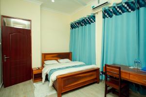 a bedroom with a bed and a desk and blue curtains at La Casa Preciosa in Tanga