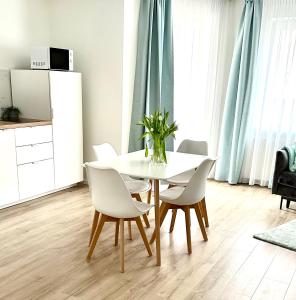 Biały stół jadalny z białymi krzesłami i wazonem na nim w obiekcie AL-DOM apartamenty Olymp 109 w Kołobrzegu