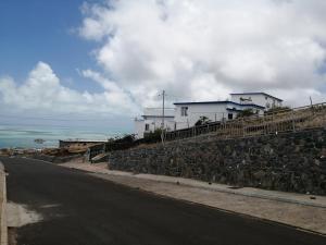 un muro di pietra accanto a una strada con una casa di Ô Bercail du Sud chez Jeannette a Rodrigues Island
