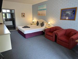 a bedroom with a bed and two red chairs at Statesman Motor Inn in Ararat