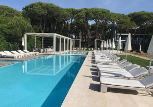 una piscina con tumbonas blancas y árboles en Hotel Mediterraneo Suite&Residence, en Lido di Jesolo