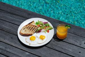 a plate of eggs and toast with salad and a glass of juice at ZIN Berawa Villas & Bungalows in Canggu