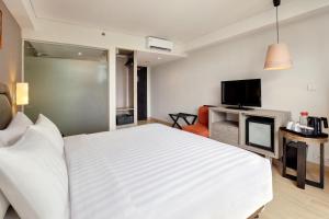a bedroom with a large white bed and a television at Harper Kuta Hotel by ASTON in Legian
