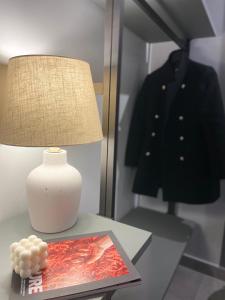 eine Lampe auf einem Tisch mit einer Zeitschrift und einem Mantel auf einem Kleiderständer in der Unterkunft Soha Piazza Di Spagna Boutique in Rom