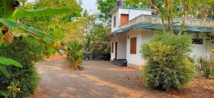 a small white house with trees and a dirt road at Kuttickattil Pool Home Stay Kumarakom in Kumarakom