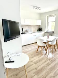 a white kitchen with a table and a tv at AL-DOM apartamenty Grey 112 Olymp in Kołobrzeg