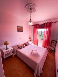 a bedroom with a bed with pink walls and a window at Cantinho dos avós in Fuzeta