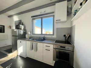 eine Küche mit weißen Schränken, einem Waschbecken und einem Fenster in der Unterkunft La Petite Échappée - Proche mer in La Genilliere
