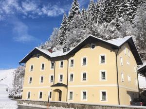 a yellow building in the snow with trees at Appartements Feroli in Dienten am Hochkönig