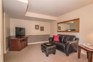 a living room with a leather couch and a flat screen tv at Auberge du Lac Morency in Saint-Hippolyte