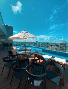 une terrasse avec une table, des chaises et un parasol dans l'établissement Edifício Promenade II Apt 1108 -Mandi Hospitalidade, à Maceió